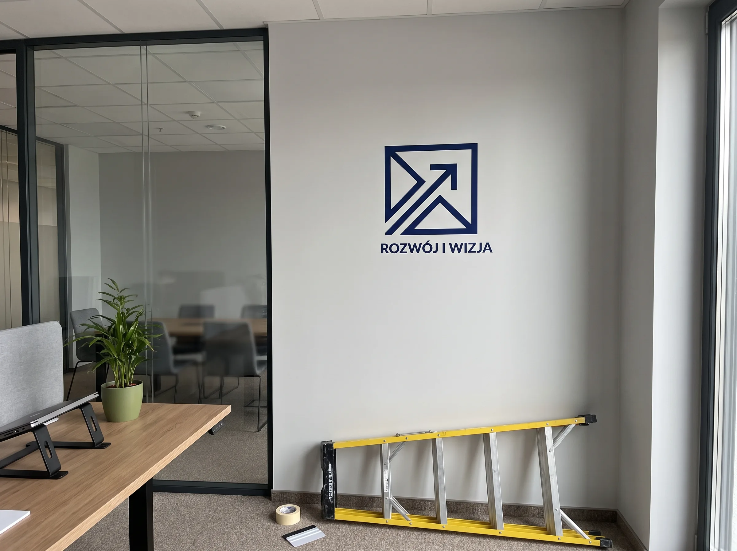 Logo 'ROZWÓJ I WIZJA' w kolorze niebieskim na białej ścianie nowoczesnego biura