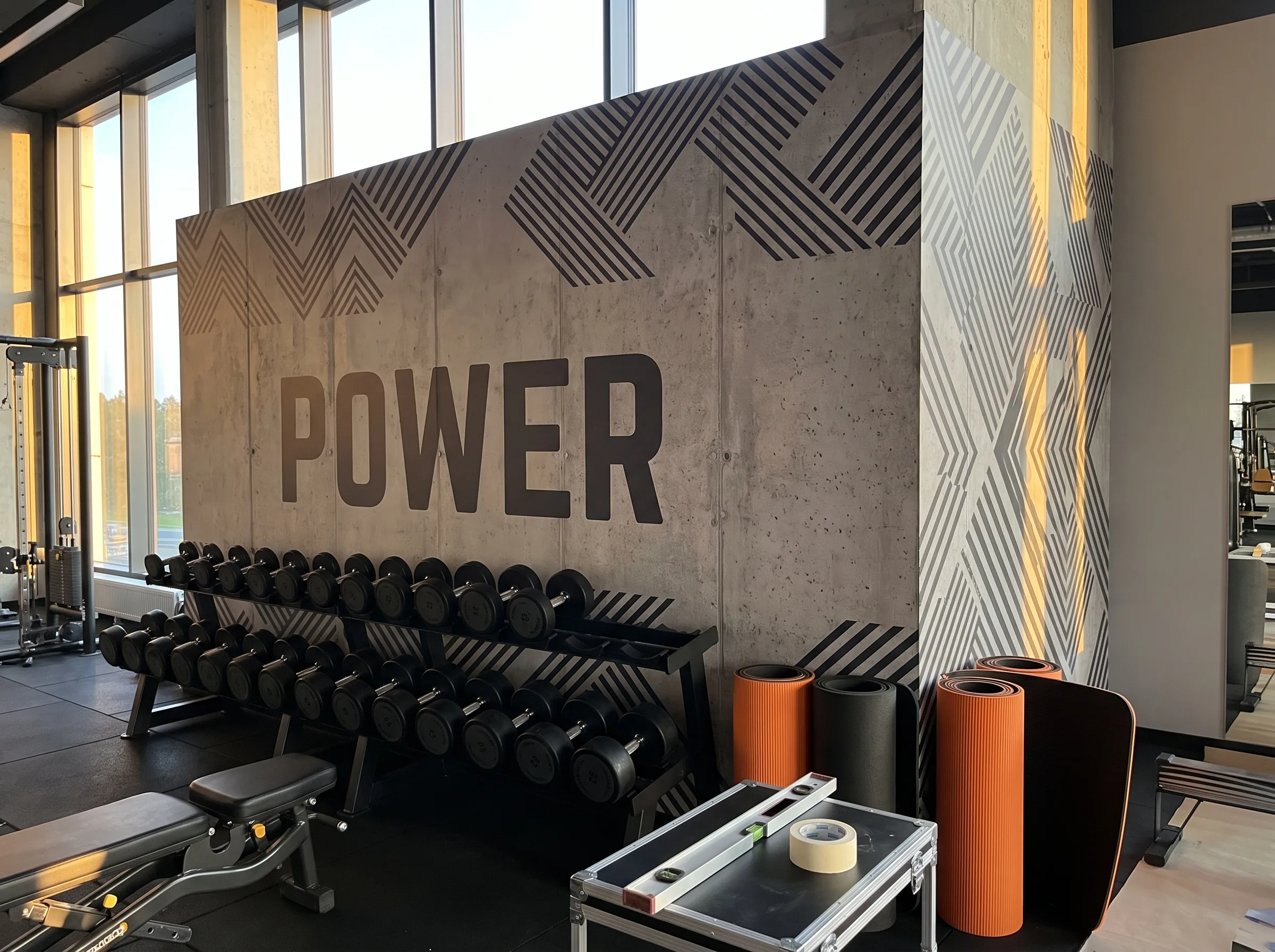 Napis POWER na betonowej ścianie z geometrycznymi wzorami w wnętrzu klubu fitness