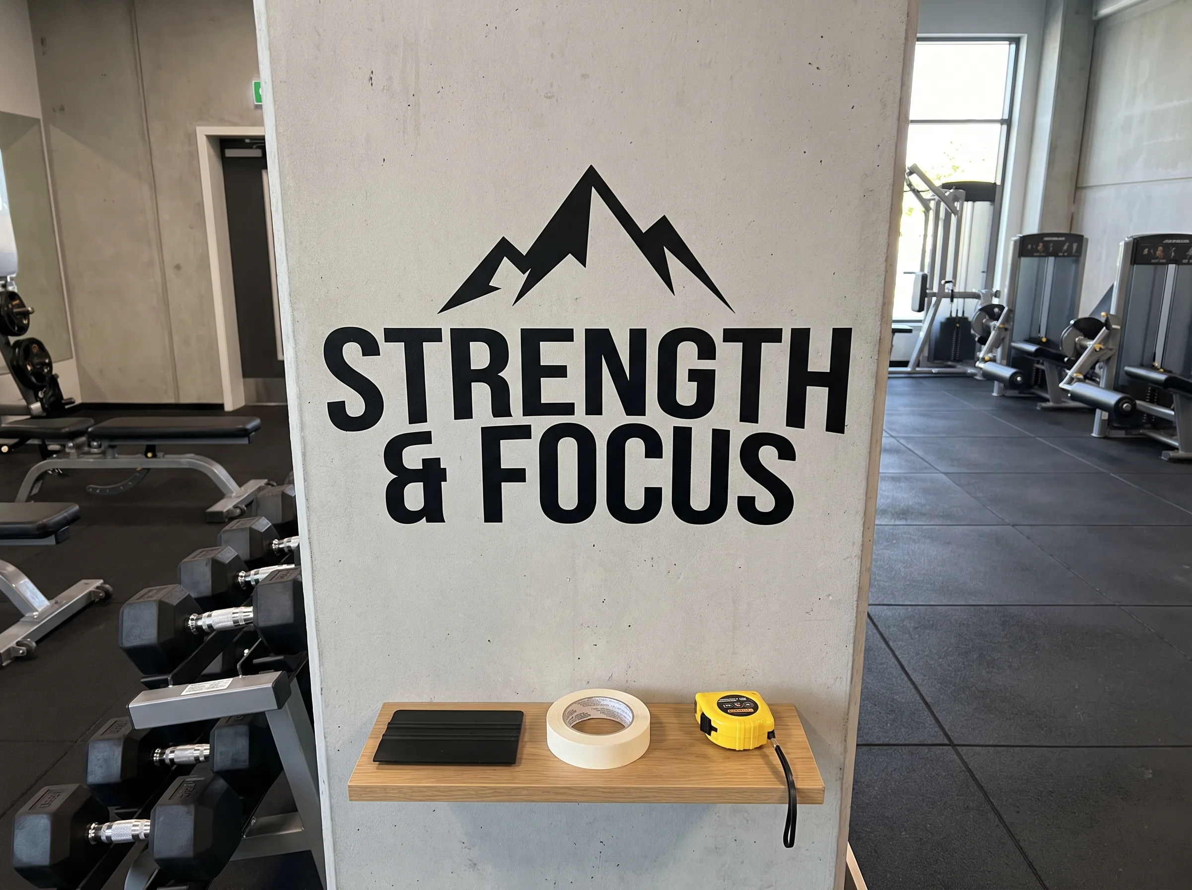 Grafika ścienna z motywacyjnym napisem i górskim szczytem w sali fitness