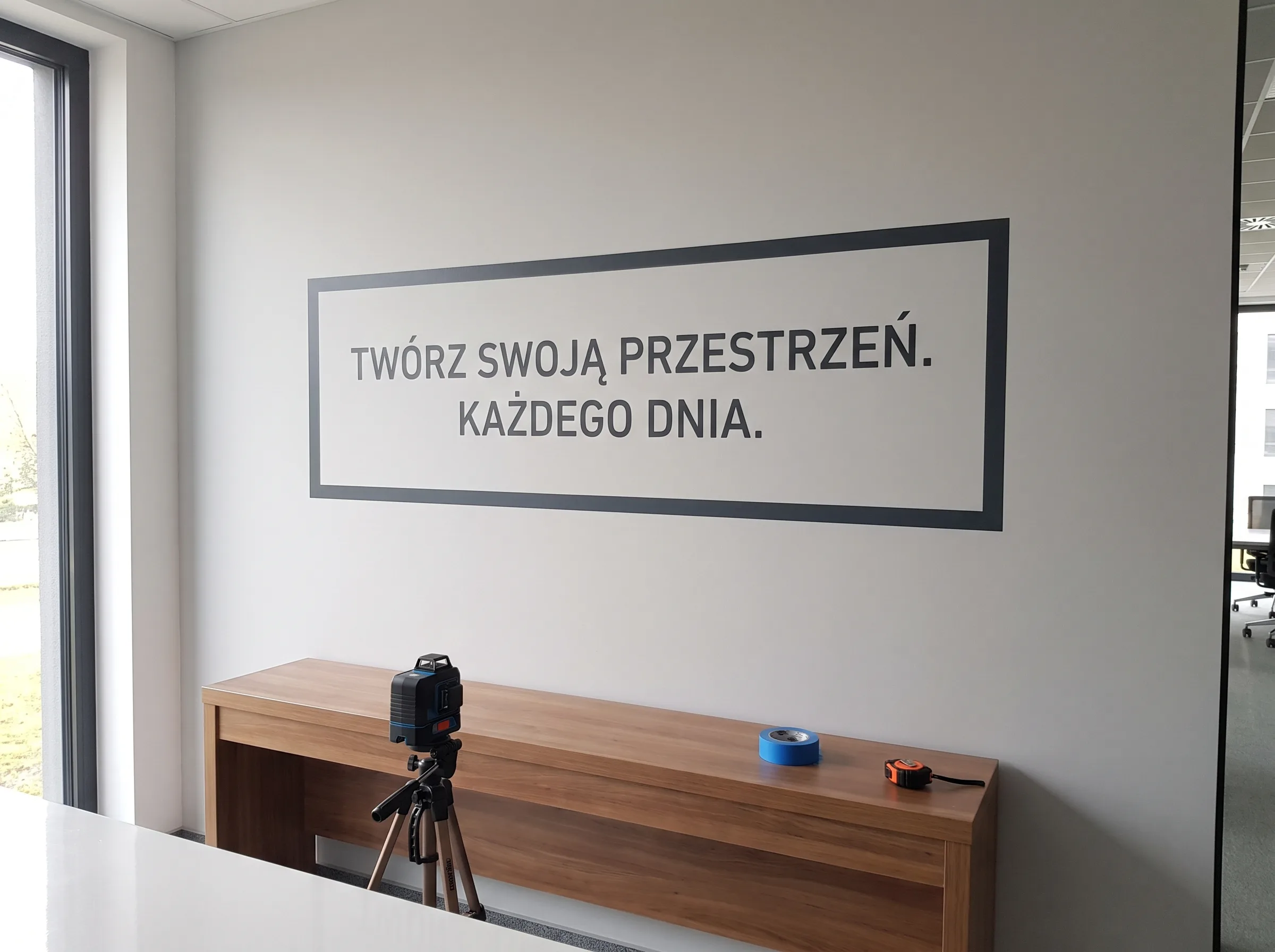 Grafika na ścianie w czarnej ramie nad drewnianym biurkiem w nowoczesnym biurze
