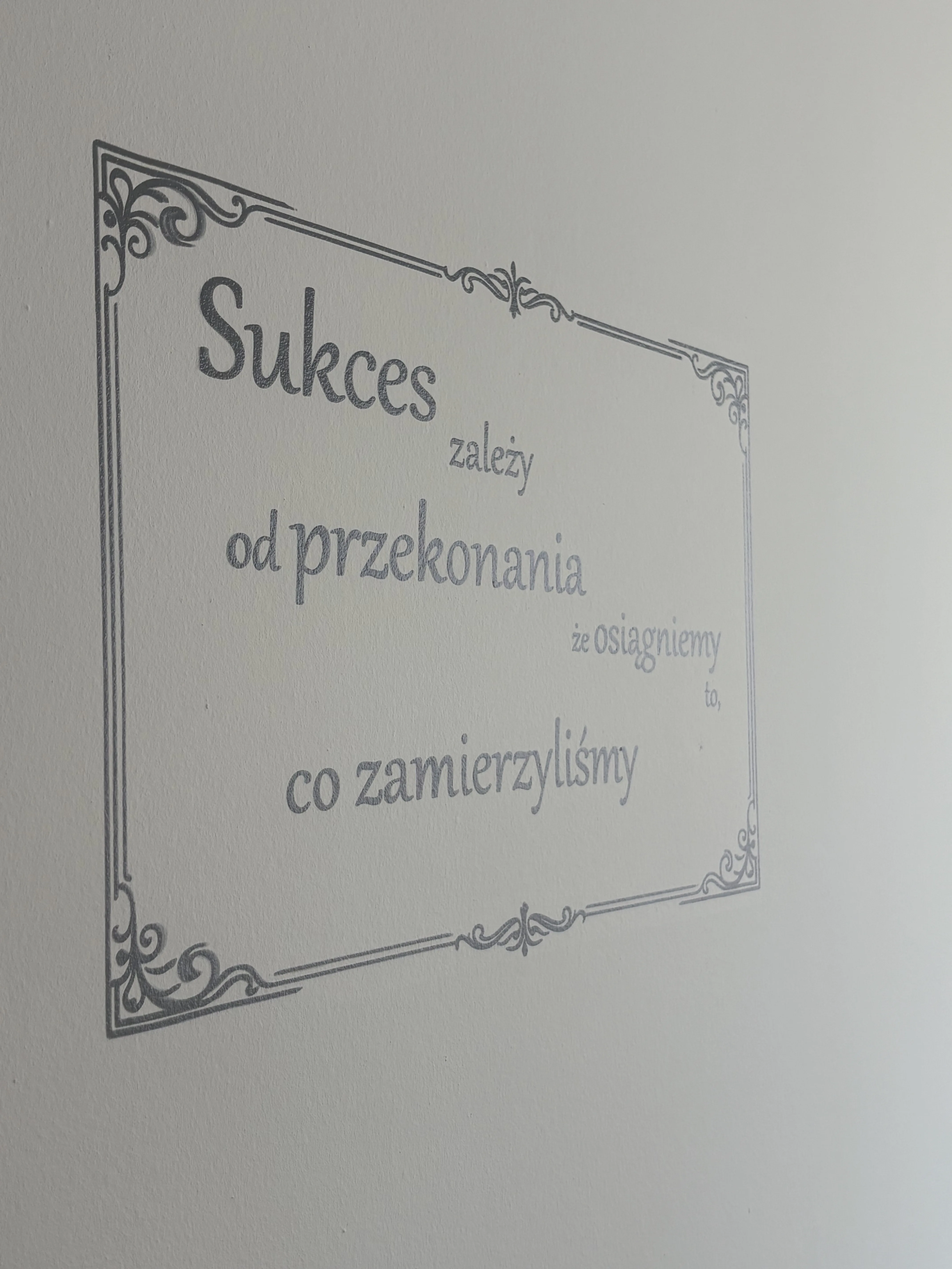Napisy na ścianie z motywacyjnym cytatem w ozdobnej ramie